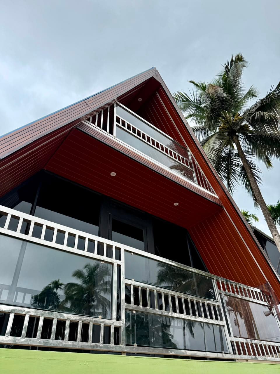 The steep timber pitch of a chalet seen from below against the coconut palms