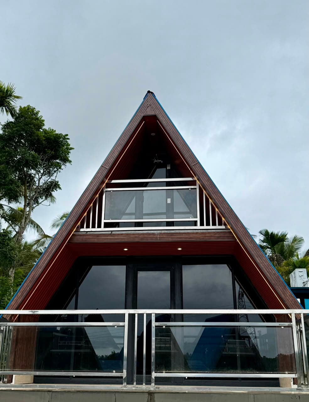 An A-frame chalet head-on, its roof line picked out in warm LED